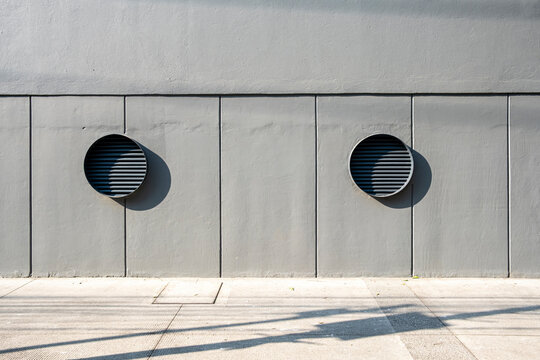 Minimalist concrete wall with circular vents, geometric lines and shadow patterns in urban architecture, ideal for design, background, and architectural stock visuals.