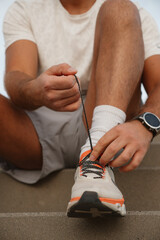 Close-up of a male athlete tying shoelaces on running shoes, focused on preparing for an outdoor...