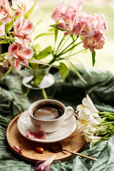 A cozy morning scene featuring a cup of coffee, flower petals, and a wooden tray. Perfect for concepts related to relaxation, lifestyle, and morning rituals.
