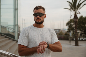 Fototapeta premium Young male athlete checking performance data on his smartwatch while wearing futuristic sunglasses in a city environment