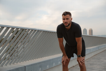 Exhausted male athlete resting on a bridge after an intense run, catching his breath and reflecting...