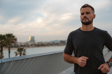 Fototapeta premium Motivated athlete jogging on a bridge, showcasing the stunning Barcelona skyline against a backdrop of the evening sky and ocean