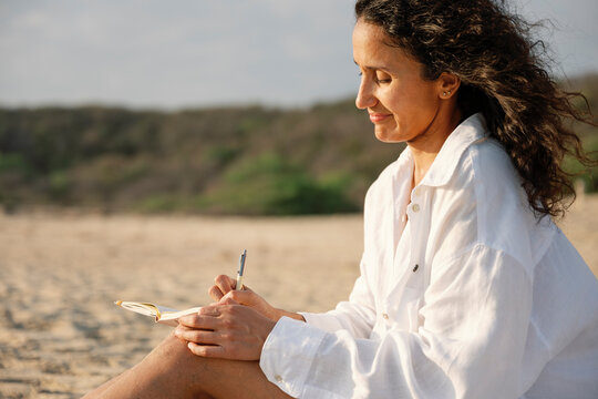 Woman writing in a notebook on a sunny beach