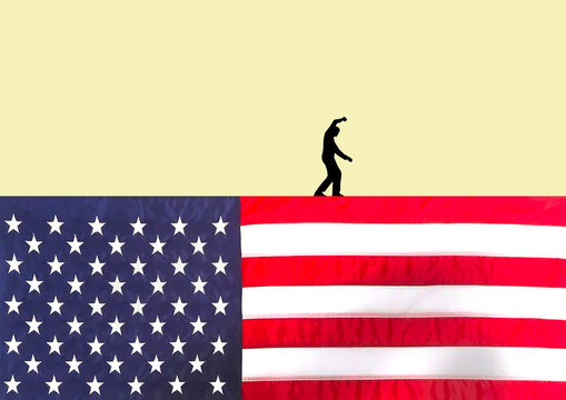 Silhouette of a person walking on the edge of a U.S. flag symbolizing balance and uncertainty in American politics and economy