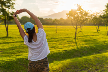 Asian woman stretching after running and training outdoors at sunset. Healthy happy girl relaxing after outdoor exercise, running workout or fitness training concept.