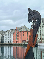 Viking figurehead of a ship prow ornament docked in the Brosundet canal, with colorful Art Nouveau buildings of Alesund, Norway reflected in the calm water