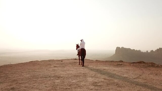 Arabian horseman gazing enless desert horizon from high plateau, dolly in shot