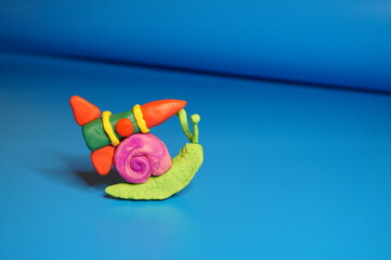 A toy snail made of plasticine with a rocket on a blue background.
