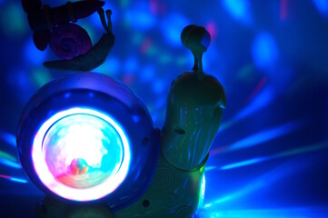 A snail with a plasticine rocket is located on another glowing toy snail. Blue background.