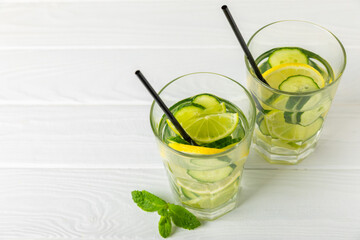 Cucumber water with lemon, lime and mint on a wooden table. Water infused with sliced ​​cucumber in a drinking glass. Tonic refreshing drink. Cucumber lemonade.Summer natural cooling drink.Copy space