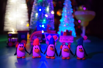 Toy penguins made of plasticine on the background of Christmas decorations.