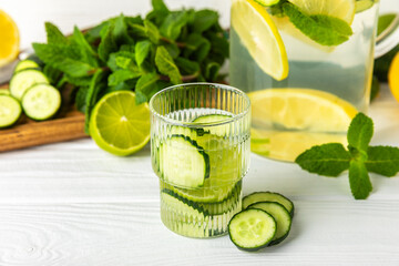 Cucumber water with lemon, lime and mint on a wooden table. Water infused with sliced ​​cucumber in a drinking glass. Tonic refreshing drink. Cucumber lemonade.Summer natural cooling drink.Copy space