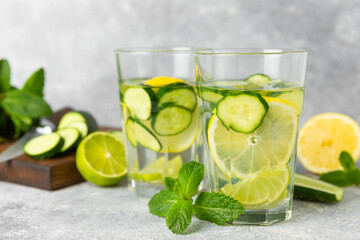 Cucumber water with lemon, lime and mint on a wooden table. Water infused with sliced ​​cucumber in a drinking glass. Tonic refreshing drink. Cucumber lemonade.Summer natural cooling drink.Copy space