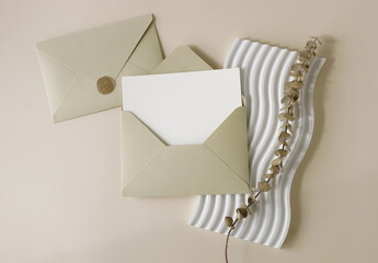 Beige envelopes with blank paper card mockup  inside top view, decor and dry eucalyptus branch on beige background. Copy space.Wedding invitation mockup, greeting card, holiday concept.