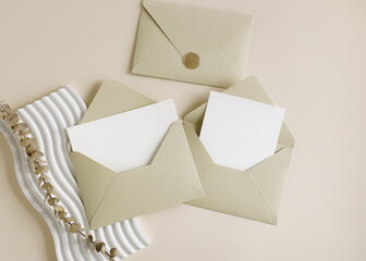 Beige envelopes with blank paper cards mockup  inside top view, decor and dry eucalyptus branch on beige background. Copy space.Wedding invitation mockup, greeting card, holiday concept.