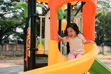 Joyful little girl sliding down a bright playground slide