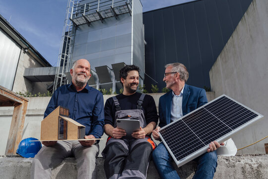Engineers discussing sustainable energy solutions outdoors with a model house and solar panel