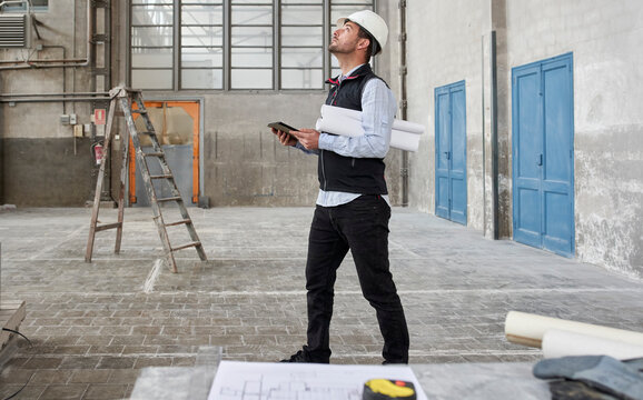 Male architect with digital tablet looking up while standing in constructing building