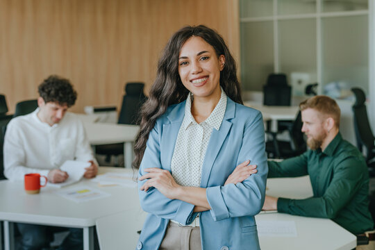 Businesswoman smiling confidently in an office with colleagues working in the background
