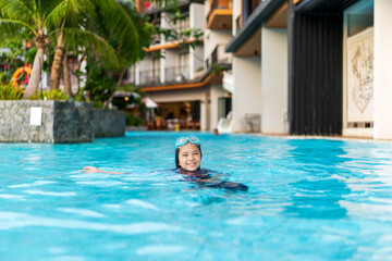 summer Asian child smile in swimming pool or young kid girl fun playing water in waterpark wear swimming goggles or people learning swim sports exercise at school or holiday vacation travel at hotel
