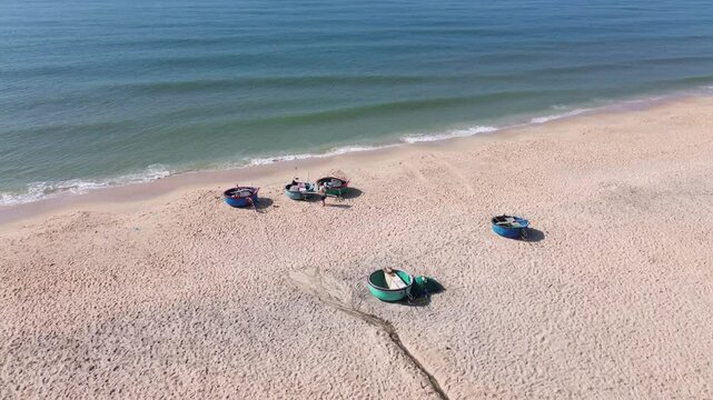 Drone flies half-circle from right to left over Mui Ne beach, keeping buckets and people walking in center, revealing resorts, white sand shore, and sea horizon.