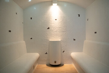Modern Steam Room Interior.Clean and minimalistic steam room with tiled walls and benches, featuring soft lighting and a central water fixture.