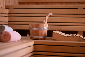 Sauna Bucket and Towels Close Up.Detailed close up of sauna bucket with ladle and essential oils next to rolled towels on wooden bench inside sauna.