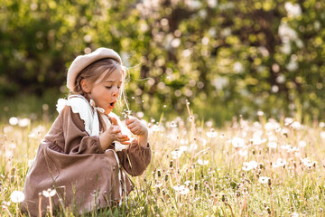 Vintage women's accessories and retro-style clothing. A small, beautiful girl with bows in her hair, in a beige dress and a beret outdoors.