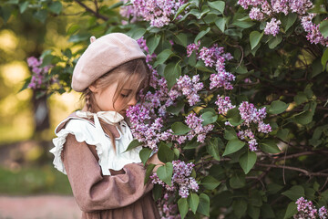 Vintage women's accessories and retro-style clothing. A small, beautiful girl with bows in her hair, in a beige dress and a beret outdoors.