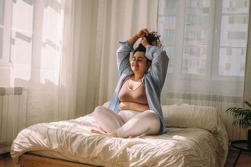 Portrait of a happy young plus-sized caucasian woman in bed. The woman has just woken up and is...