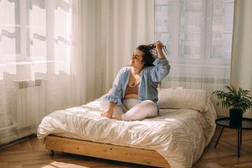Portrait of a happy young plus-sized caucasian woman in bed. The woman has just woken up and is stretching.Healthy lifestyle.