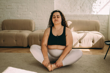 A young curly-haired plus-size woman meditates at home,sitting in the lotus position.Healthy lifestyle.