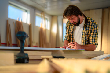 Focused carpenter meticulously taking notes and planning his woodwork project in a bright and organized workshop, surrounded by tools and lumber