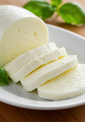 Sliced mozzarella cheese with fresh basil leaves on a white plate, ready to serve.