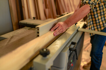 Carpenter processing a wooden plank on a thicknessing machine in a workshop, skillfully crafting furniture and other woodwork projects with precision and care
