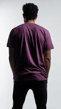 Person with curly hair, wearing a violet tshirt, posing with hands in pockets against a bright studio background.