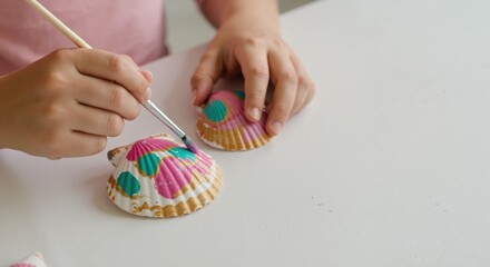 Child painting colorful shells on white table at home  