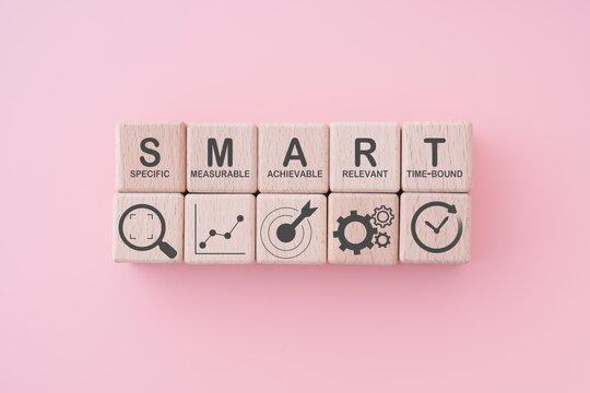 Smart goal for business strategy concept. specific, measurable, achievable, relevant and time-bound text on wooden block with icons on ping background