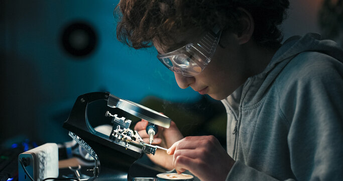 A student spends his free time at a desk, learning electronics by soldering wires. He protects his eyes and concentrates as smoke rises from the repaired connection.