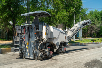 Heavy asphalt milling equipment removing pavement layer for resurfacing, roadwork preparation, infrastructure maintenance, urban construction, machinery in action, roadside environment, active site