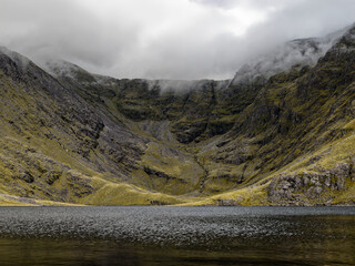 Misty mountain lake nestled in a rugged valley, a serene yet dramatic scene of nature's power and quiet beauty.