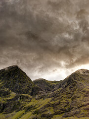 Carrauntoohil, the highest mountain in Ireland, is surrounded by swirling clouds as dusk falls. The landscape is full of green hills and rocky outcrops.