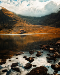 Calm waters of Lough Callee reflect the majestic mountains and clouds above during twilight. The serene landscape showcases the beauty of Ireland's natural scenery.