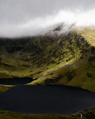 Jagged peaks pierce through swirling mist above a calm, dark lake. The scene conveys feelings of mystery and awe-inspiring natural beauty.