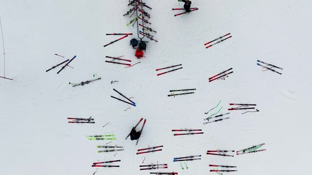 Aerial view of colorful skis scattered across the snow near a ski rack at the base of a mountain.
