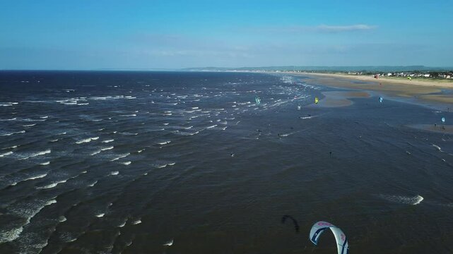 drone footage capturing people kitesurfing and flying kites along the wide sandy beaches of Normandy, France.