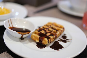 Static shot of delicious waffles with vegan chocolate sauce flowing down against a black background