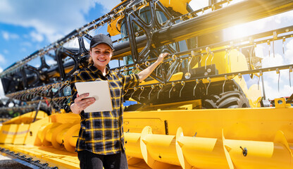 Young woman operating digital tablet near yellow combine harvester outdoors
