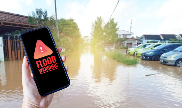 Alert symbol on smartphone over blurred flooding rains in Thailand, flood warning