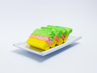 Colorful layered sponge cake in green, pink, and yellow served on a white plate with a clean white background.